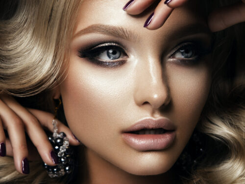 Nahaufnahme einer Frau mit Smokey Eye, Nude Lippen und violetten Fingernägeln