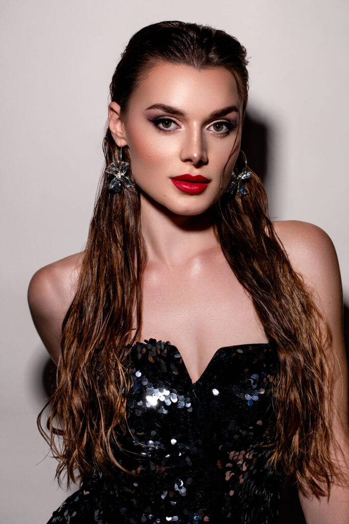 Festlicher Make-up Look mit sanftem Glow, präzisem Augen-Make-up, rotem Lippenstift und Wet-Hair-Styling im Studio fotografiert.