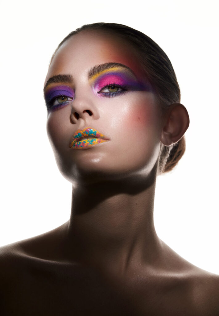Kreatives Face Design mit buntem Augen-Make-up in Pink, Lila und Gelb sowie künstlerisch gestalteten Lippen