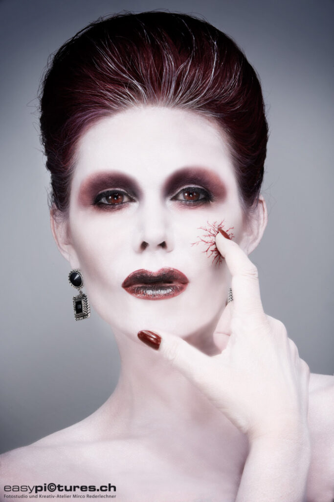 Kreatives Beauty Make-up mit heller Haut, dunklen Augen und roten Details