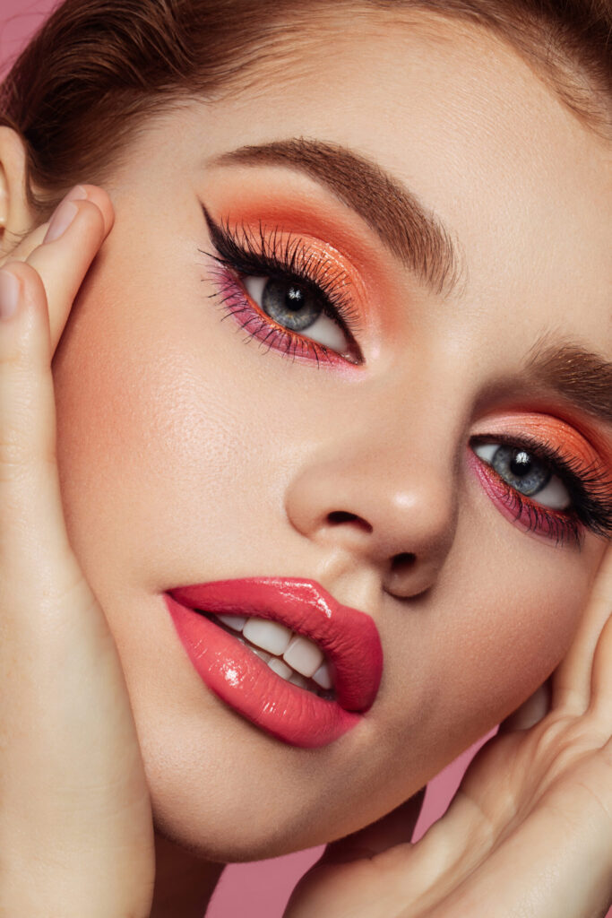 Nahaufnahme einer Frau mit orangefarbenem Augen-Make-up, Wing Eyeliner und glänzenden Lippen